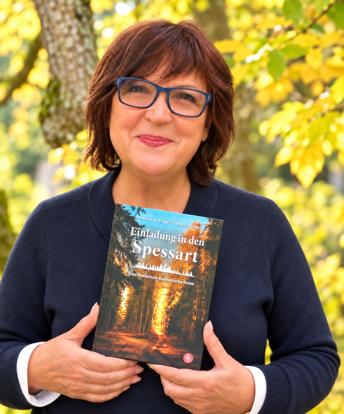 Manuela Engel-Dahan mit der Anthologie Einladung in den Spessart vor herbstlichen Bäumen